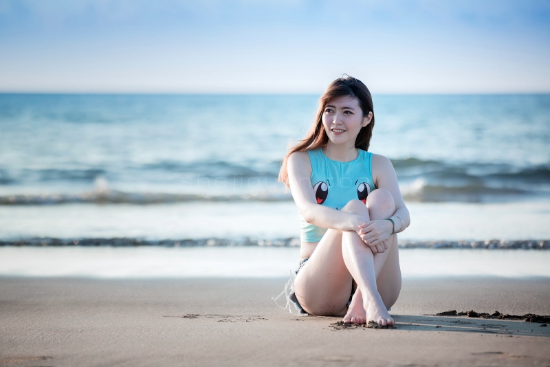 海边的沙滩上坐着一位雪白长腿的长发美女,皮肤白皙性感